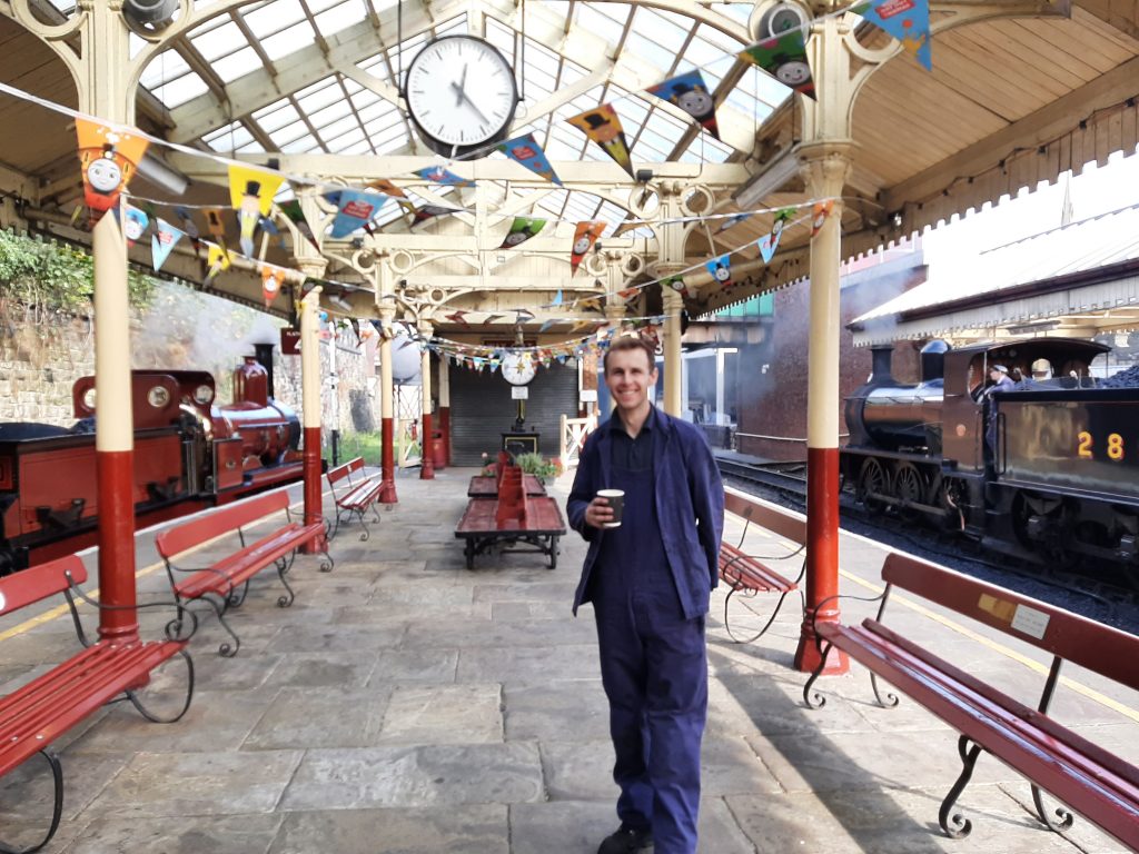 Sam with his hand around a cup of tea at Bury Bolton Street station, with FR 20 and Douglas and their respective trains.